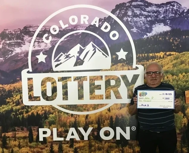 约翰·P 在科罗拉多州彩票背景前手持 $1,000的支票